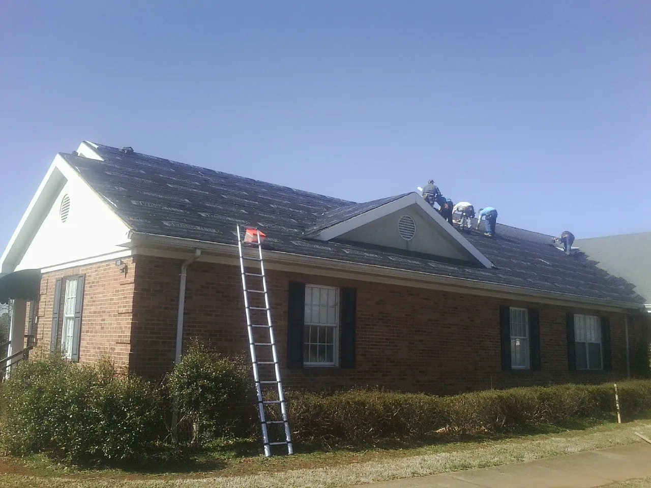 Crew tearing shingles off a brick ranch roof with a ladder set — Metal Roof Repair work by our crew in Old Fort