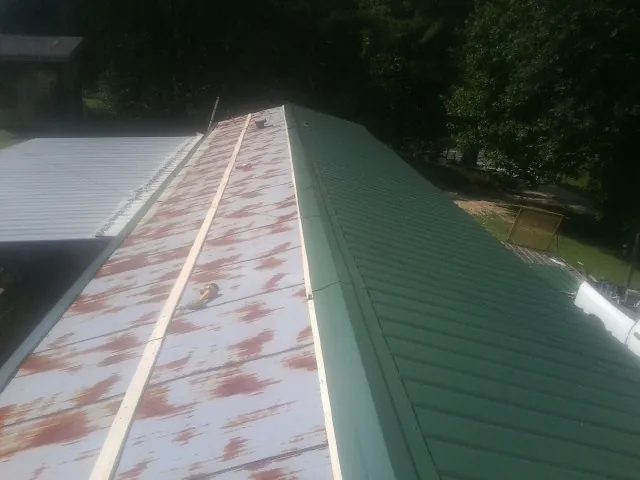Old rusted panels beside newly installed green metal roofing — Wind Damage Roof Repair by Roofing Brothers in Old Fort