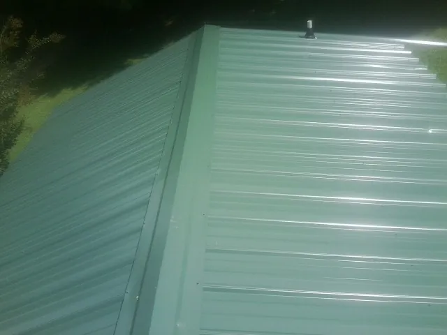 New green metal panels meeting at the ridge of a roof — Flat Roof Repair work by our crew in Old Fort