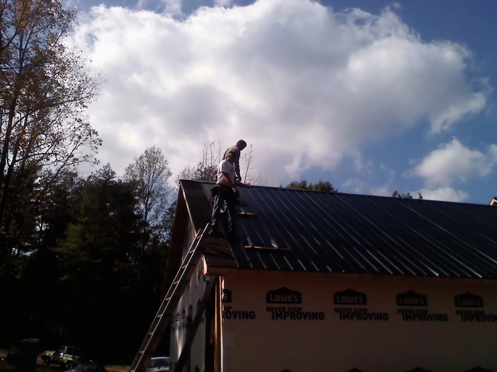 Roofer fastening dark metal panels high against a cloudy sky, from a Roof Inspection job in Old Fort