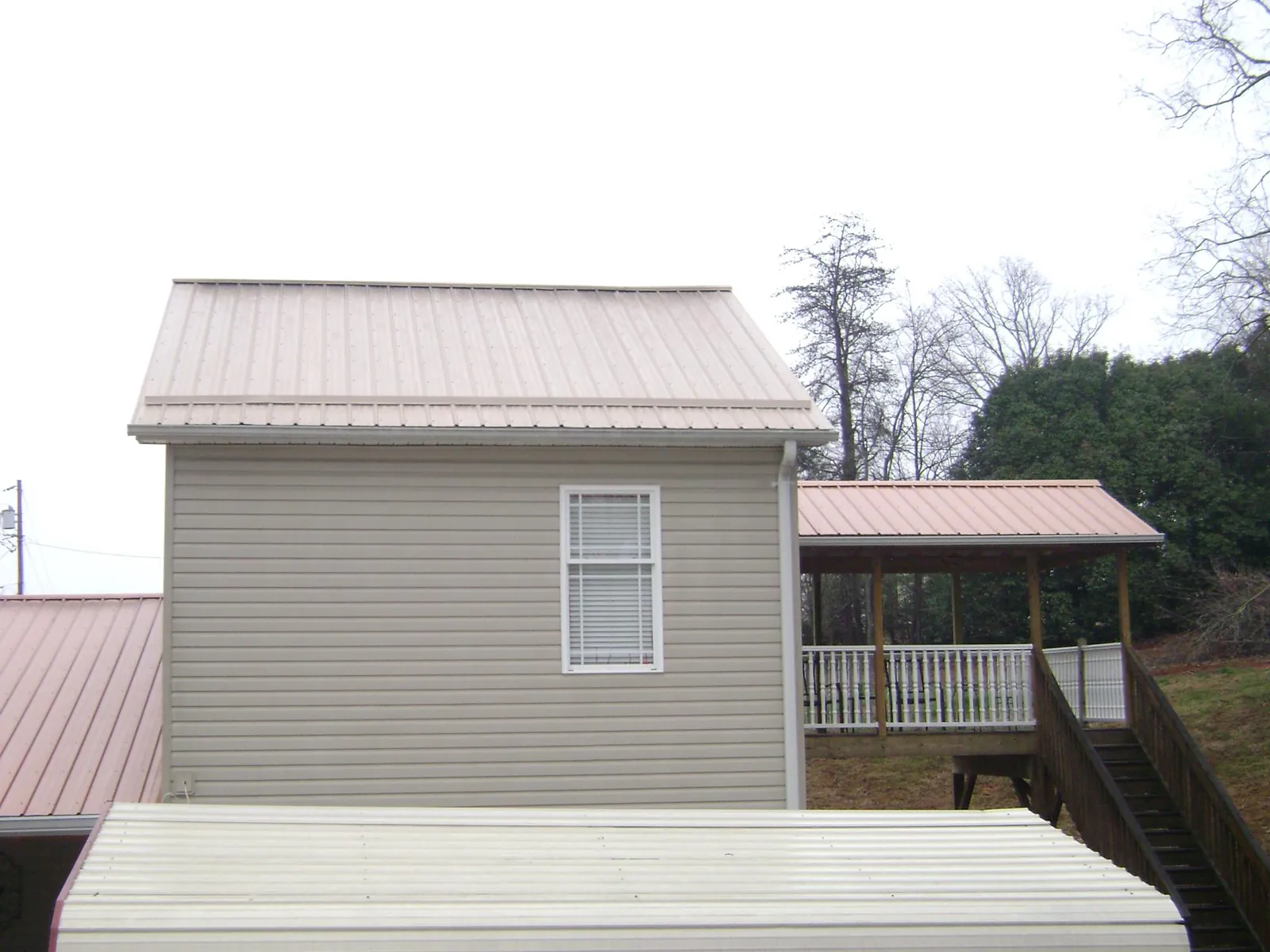 Tan metal roofs on a two story addition and attached porch, from a Roof Replacement job in Old Fort
